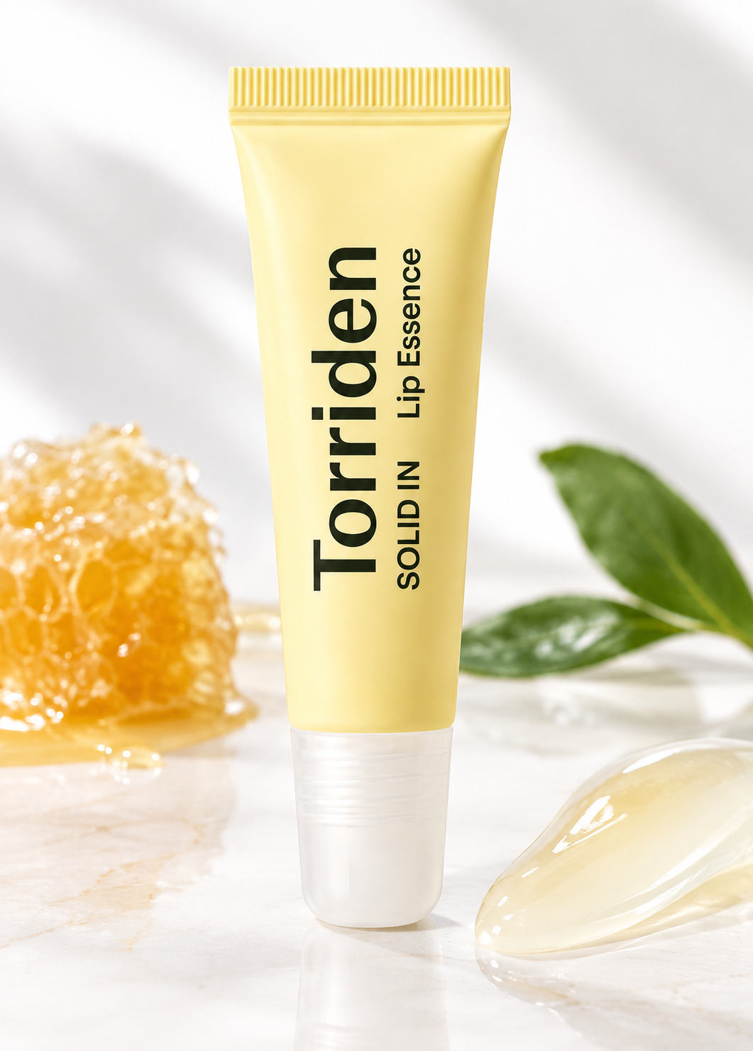 Torriden SOLID IN Lip Essence displayed in a bright, natural skincare setting with honeycomb, fresh green leaves and a glossy balm texture, highlighting its nourishing, moisture-rich lip care concept.