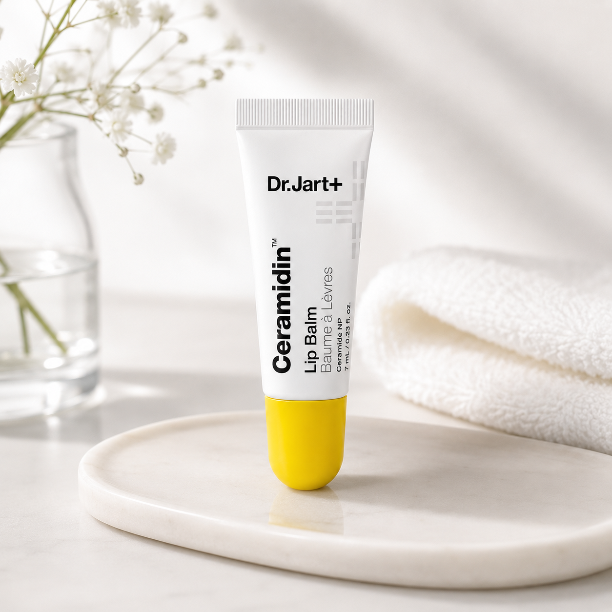 Dr.Jart+ Ceramidin Lip Balm 7ml elegantly displayed on a white marble tray in a bright spa-inspired setting with soft towels, delicate white flowers, clear glass décor and gentle natural light, highlighting intense lip hydration, barrier repair and everyday nourishment with a clean, premium Korean skincare aesthetic.