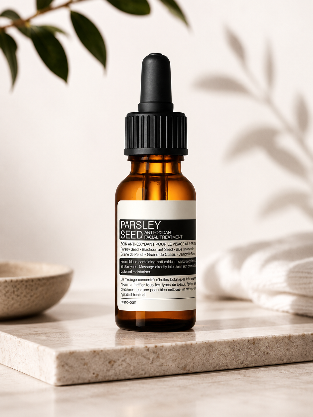 Aesop Parsley Seed Anti-Oxidant Facial Treatment displayed on a light stone countertop in a minimalist spa-inspired setting with soft natural light, botanical foliage, a ceramic bowl, and folded white towels. The elegant composition highlights the antioxidant-rich facial treatment oil as part of a premium skincare routine, emphasizing nourishment, hydration, skin protection, and Aesop's refined apothecary aesthetic.